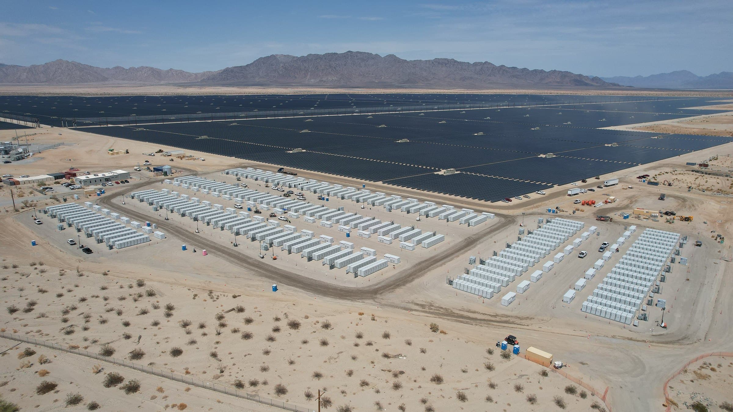 Vista aérea de usina solar no deserto com sistema de armazenamento em baterias e montanhas ao fundo.