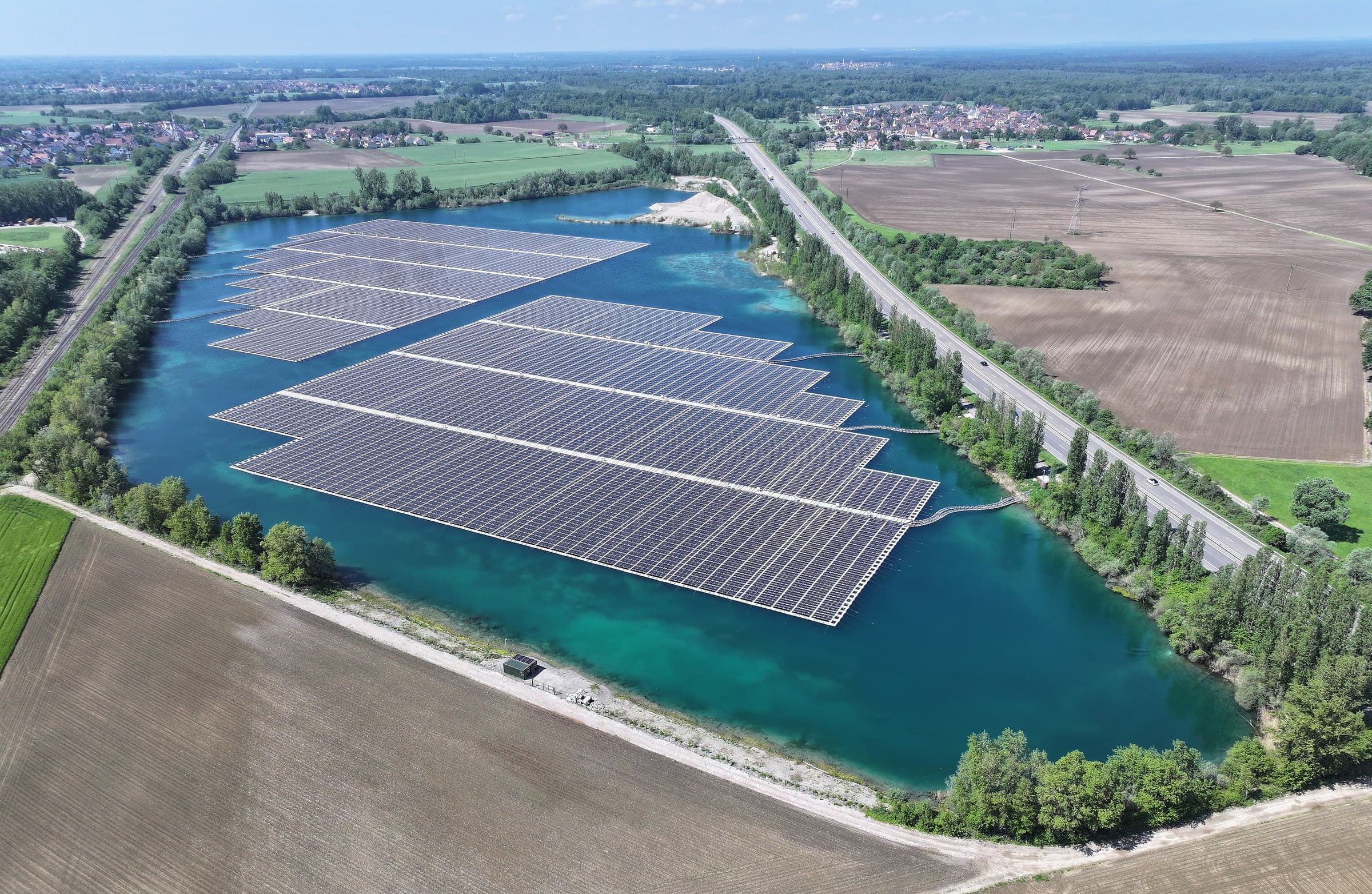 Vista aérea de usina solar flutuante em lago azul-turquesa cercado por campos.